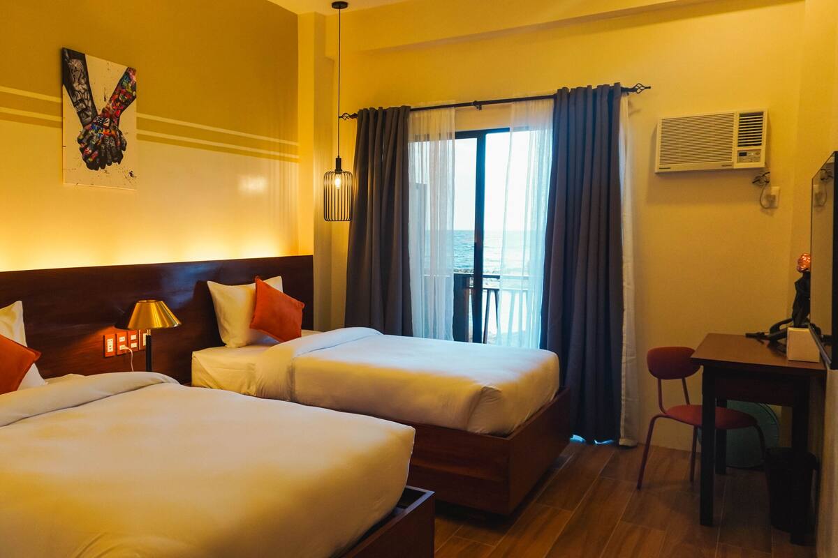 Een hotelkamer met twee bedden, een bureau, een stoel, een lamp en een raam met gordijnen.