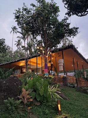 A building with a covered outdoor area, surrounded by lush greenery and palm trees. - UNWND Boutique Hotel Camiguin (Mambajao)