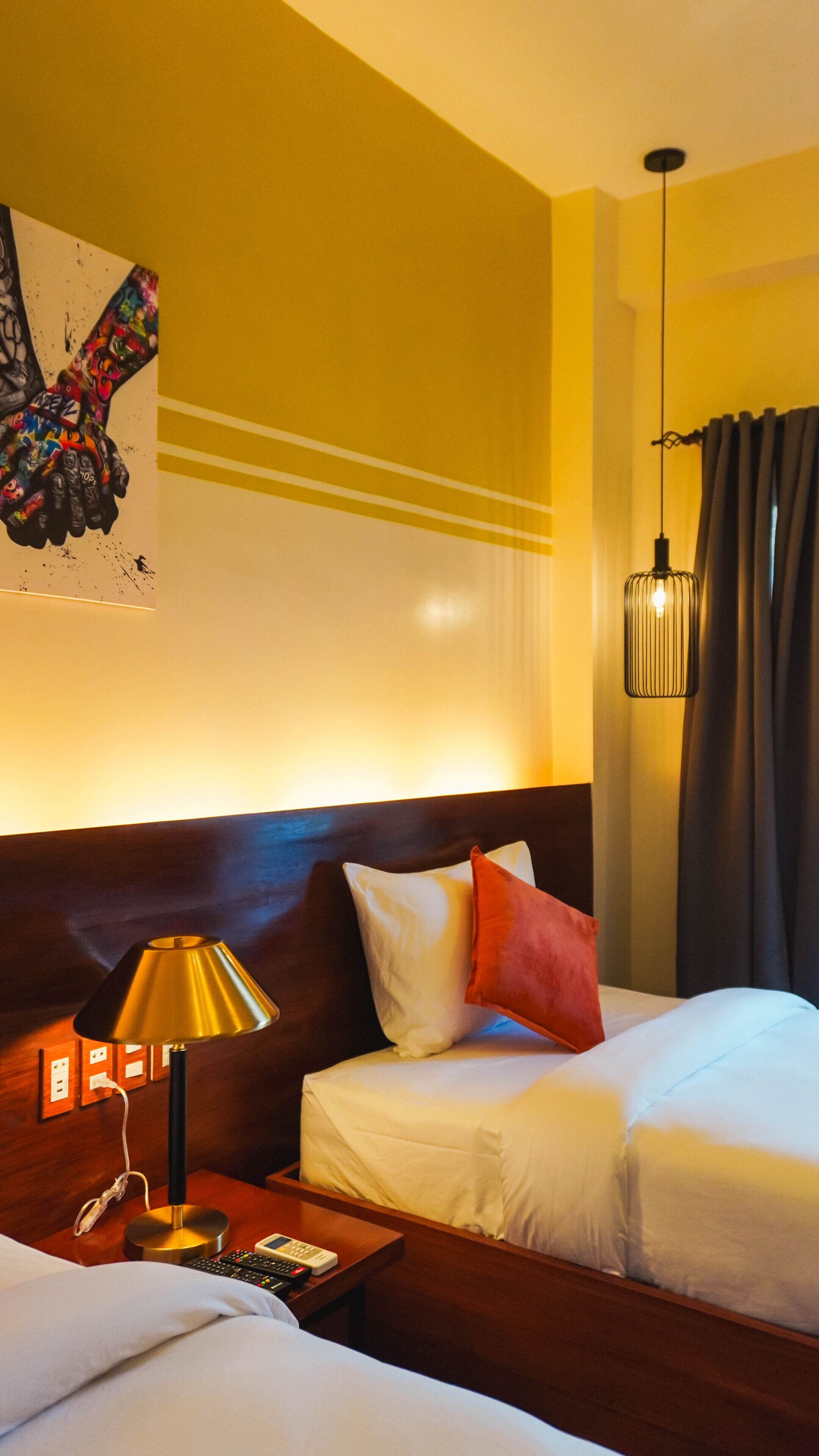 Habitació d'hotel amb dos llits, una tauleta de nit amb una làmpada, un quadre a la paret i una llum al sostre.