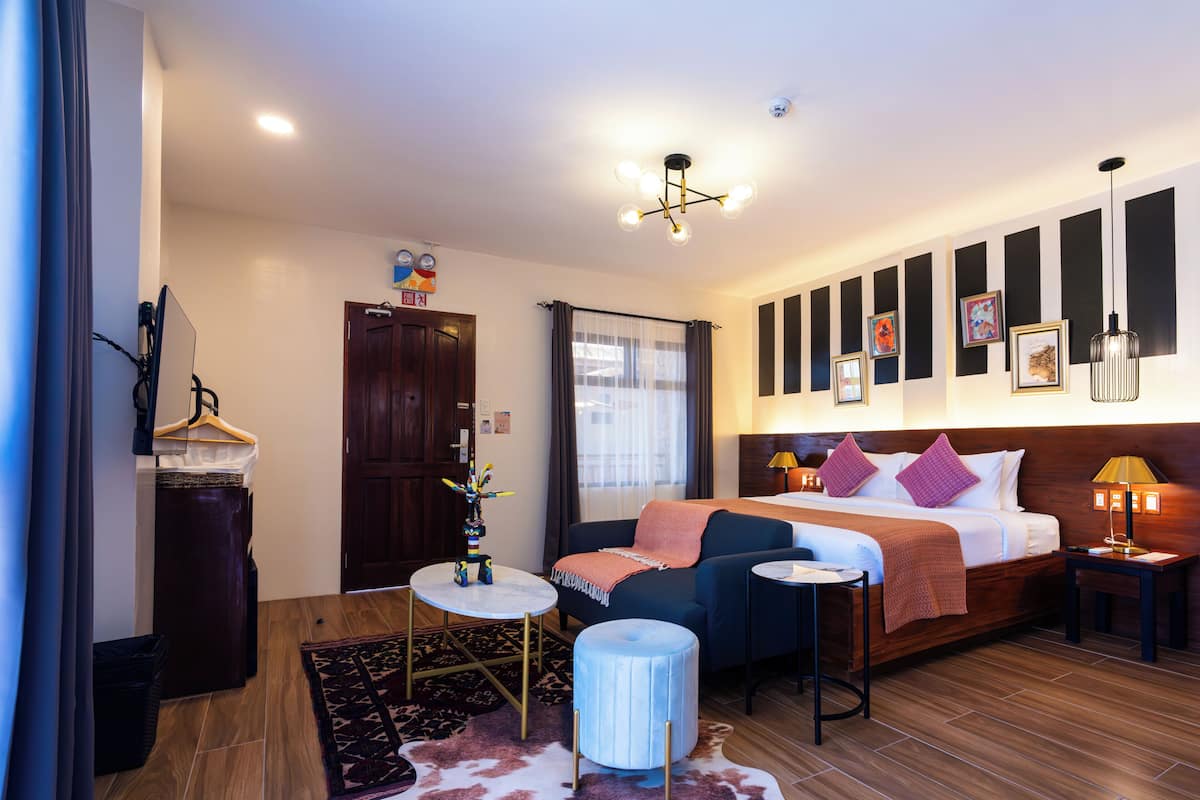 Een hotelkamer met een bed, nachtkastjes, een bureau, een stoel, een kleedje, een hangplant en een deur.