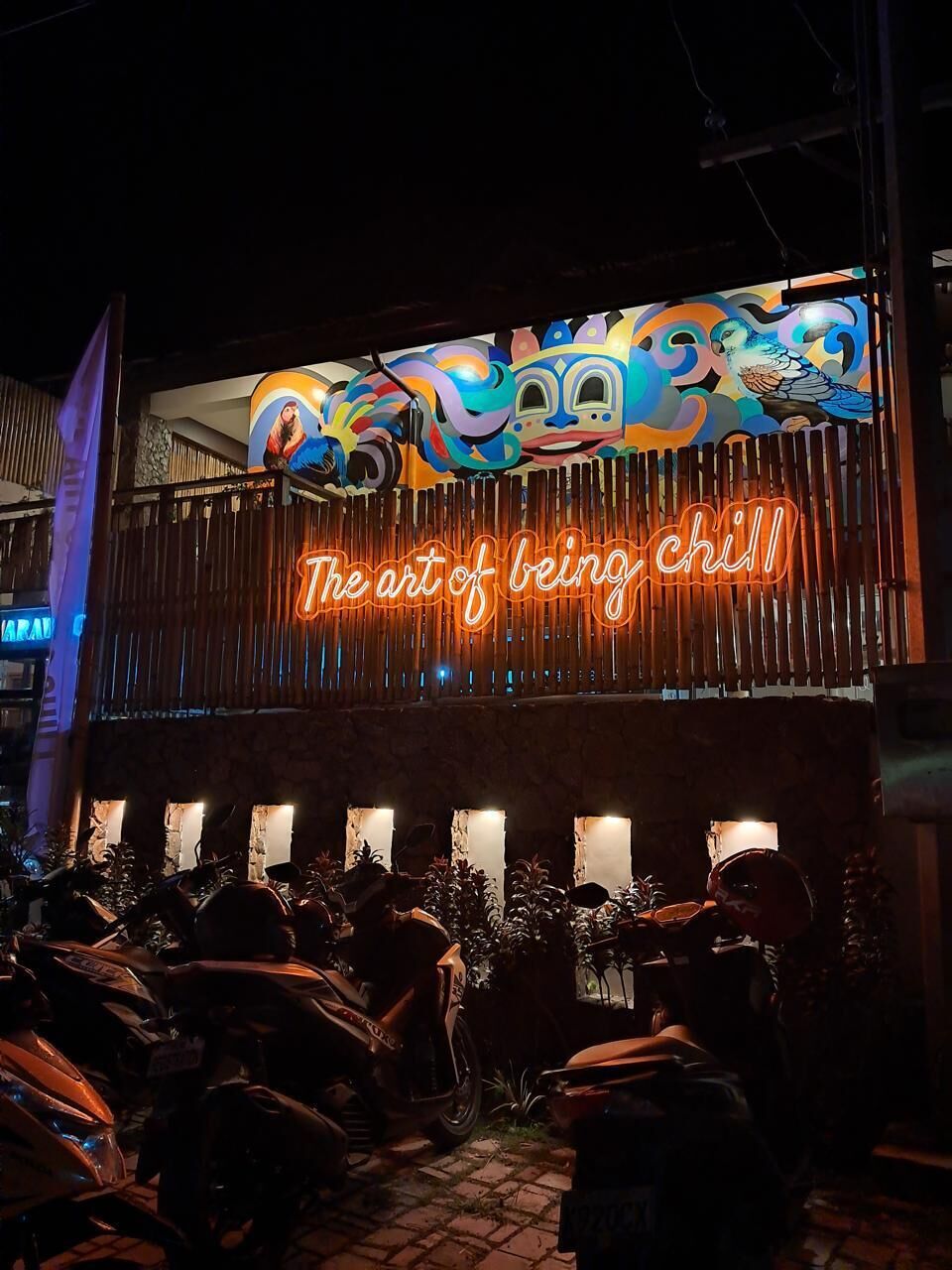 Een gebouw met een neonbord waarop staat 'The art of being chill' en motorfietsen die ervoor geparkeerd staan.