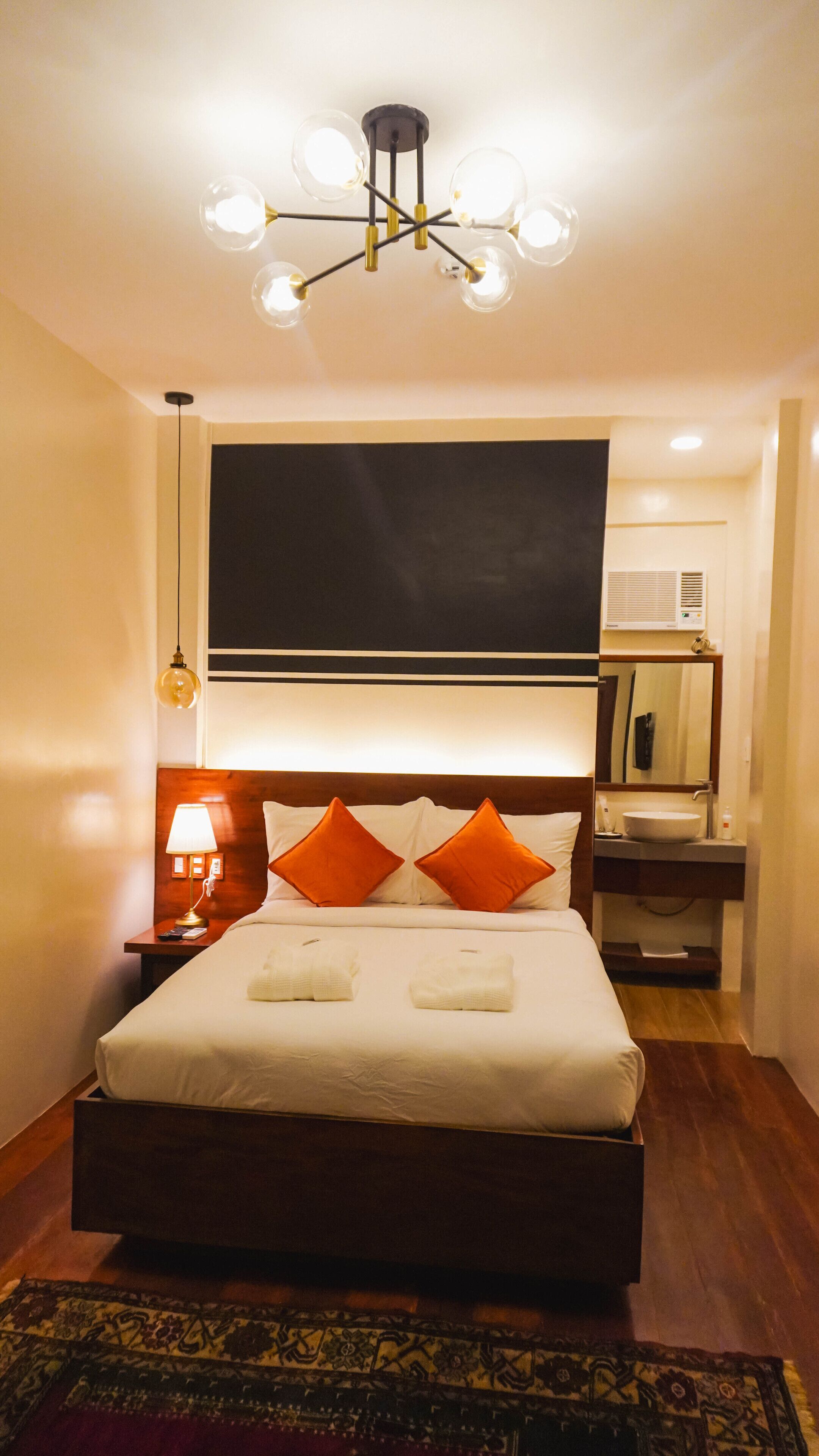 A hotel room with a large bed, a bedside table with a lamp, a mirror, and a ceiling light fixture.