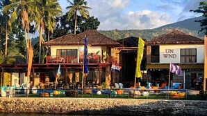 Un hotel frente al agua con varias edificaciones, mesas al aire libre y banderas.