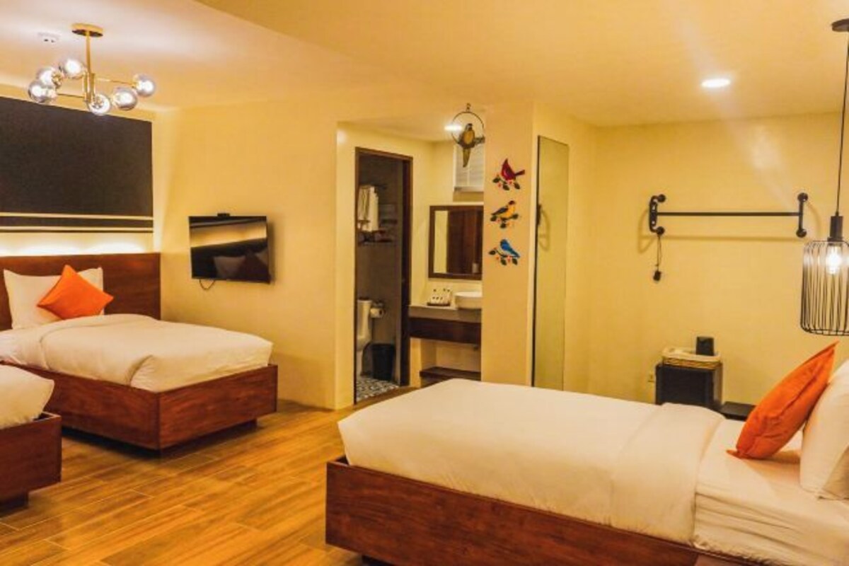 Quarto de hotel com duas camas, televisão, espelho e lustre.