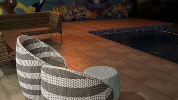 Zona de piscina con mobiliario de mimbre, un letrero de neón y un mural.