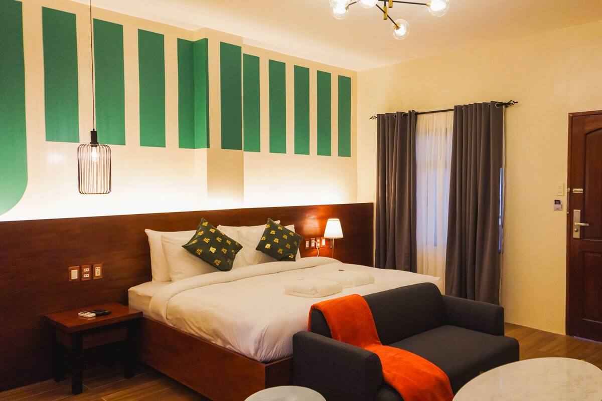 Een hotelkamer met een bed, nachtkastje, lamp en een stoel.