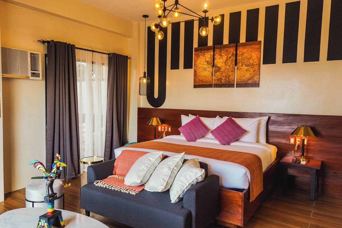 Een hotelkamer met een bed, nachtkastjes, een bank, een decoratief beeld van een vogel, een kaart aan de muur en een raam met gordijnen.