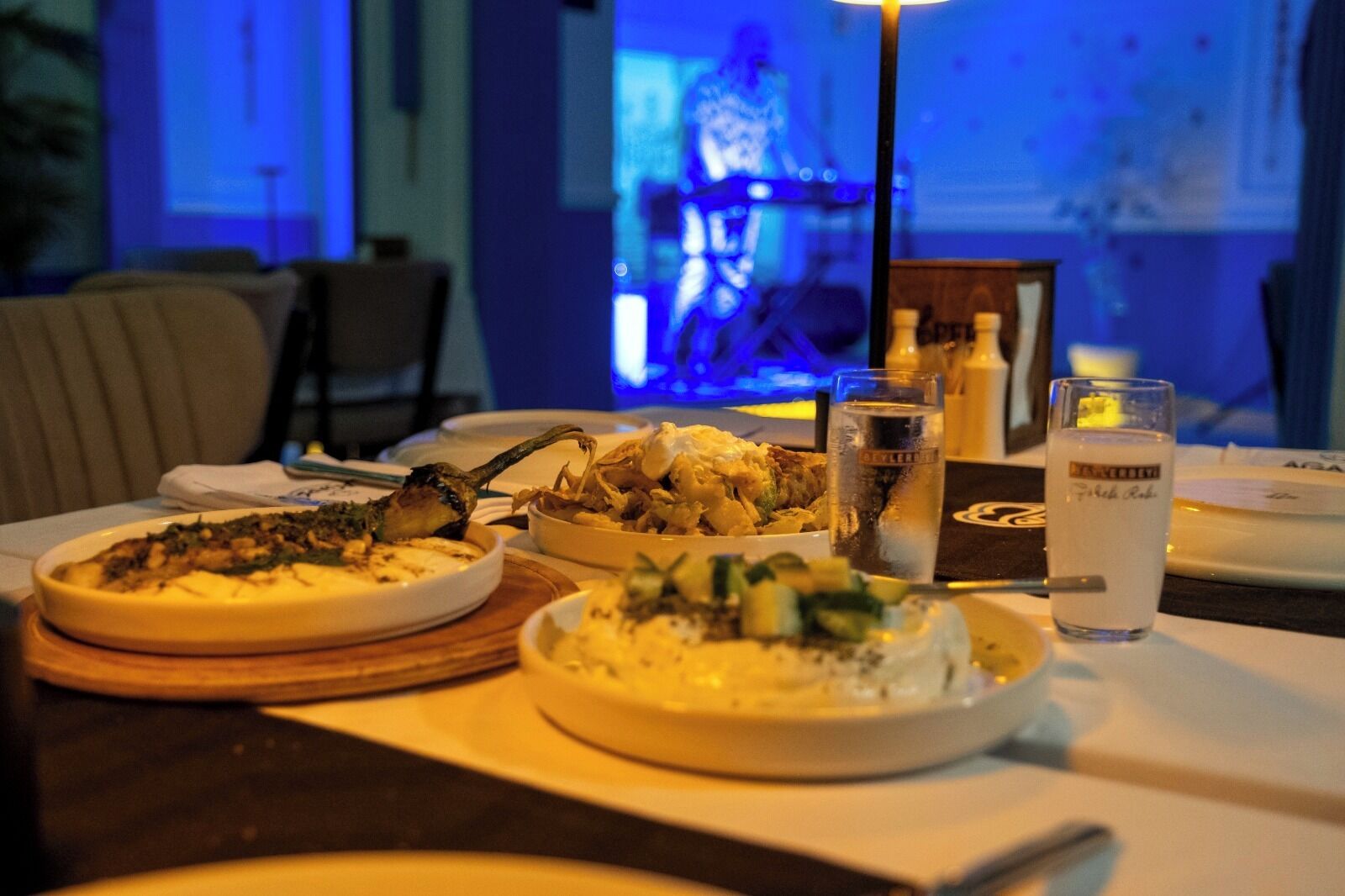 Una mesa de comedor con diferentes platos, vasos de agua y una carta.
