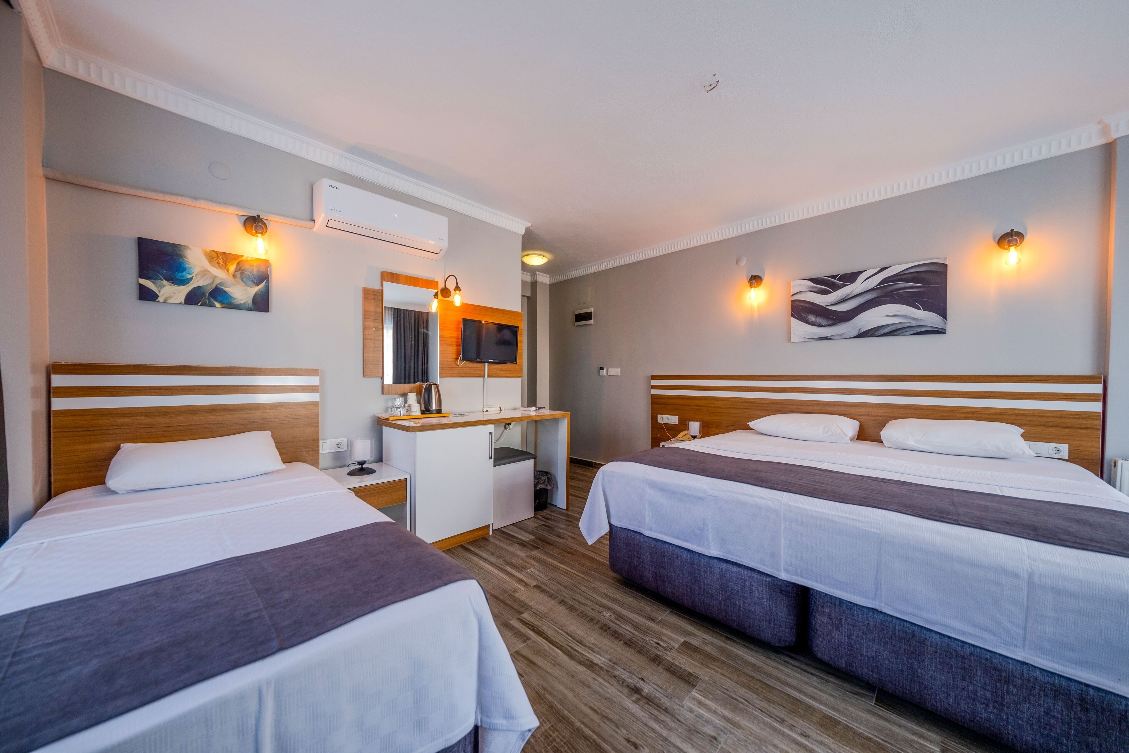 Quarto de hotel com duas camas, uma escrivaninha, um espelho e obras de arte nas paredes.