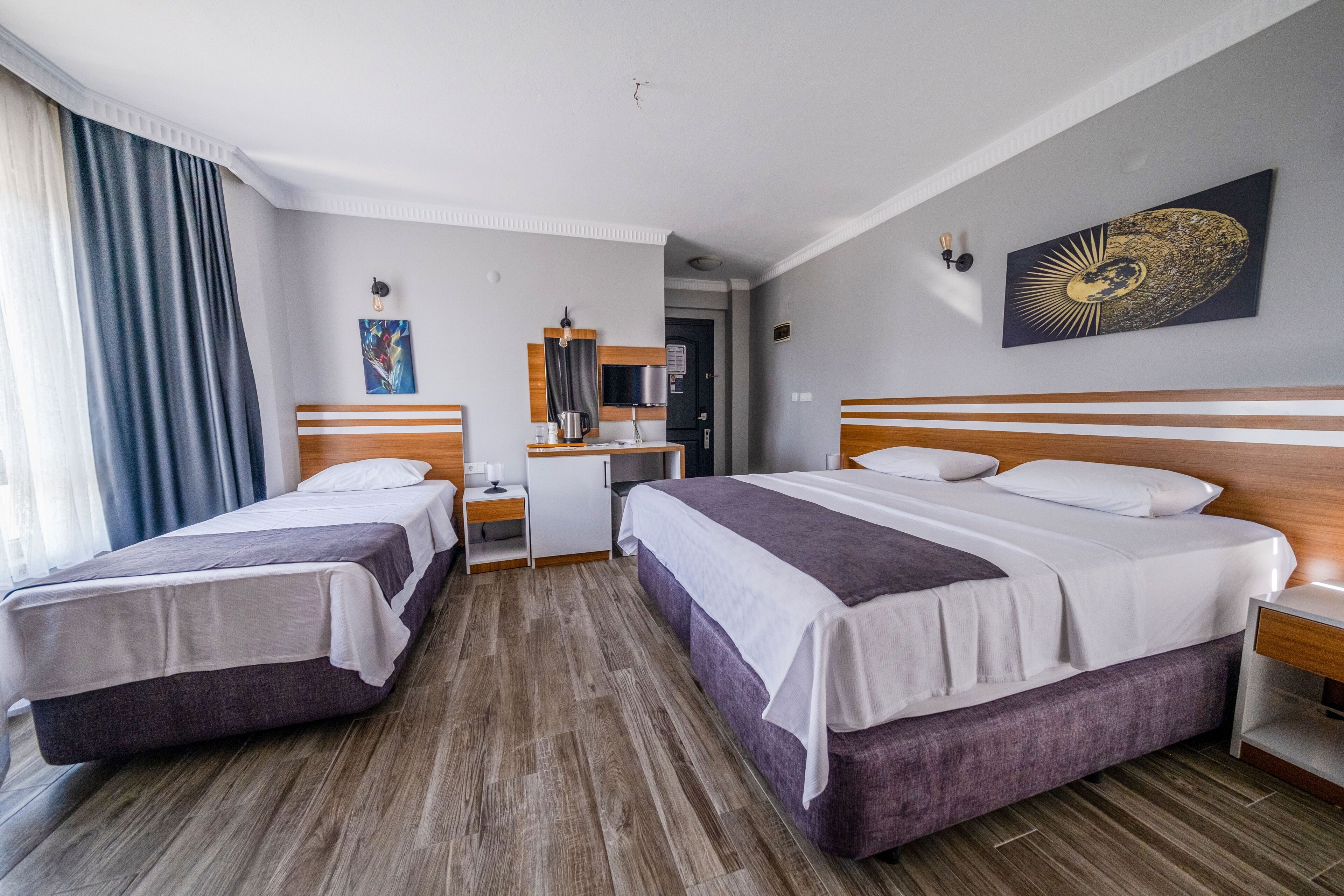 A hotel room with two beds, a desk, a mirror, and a painting on the wall.