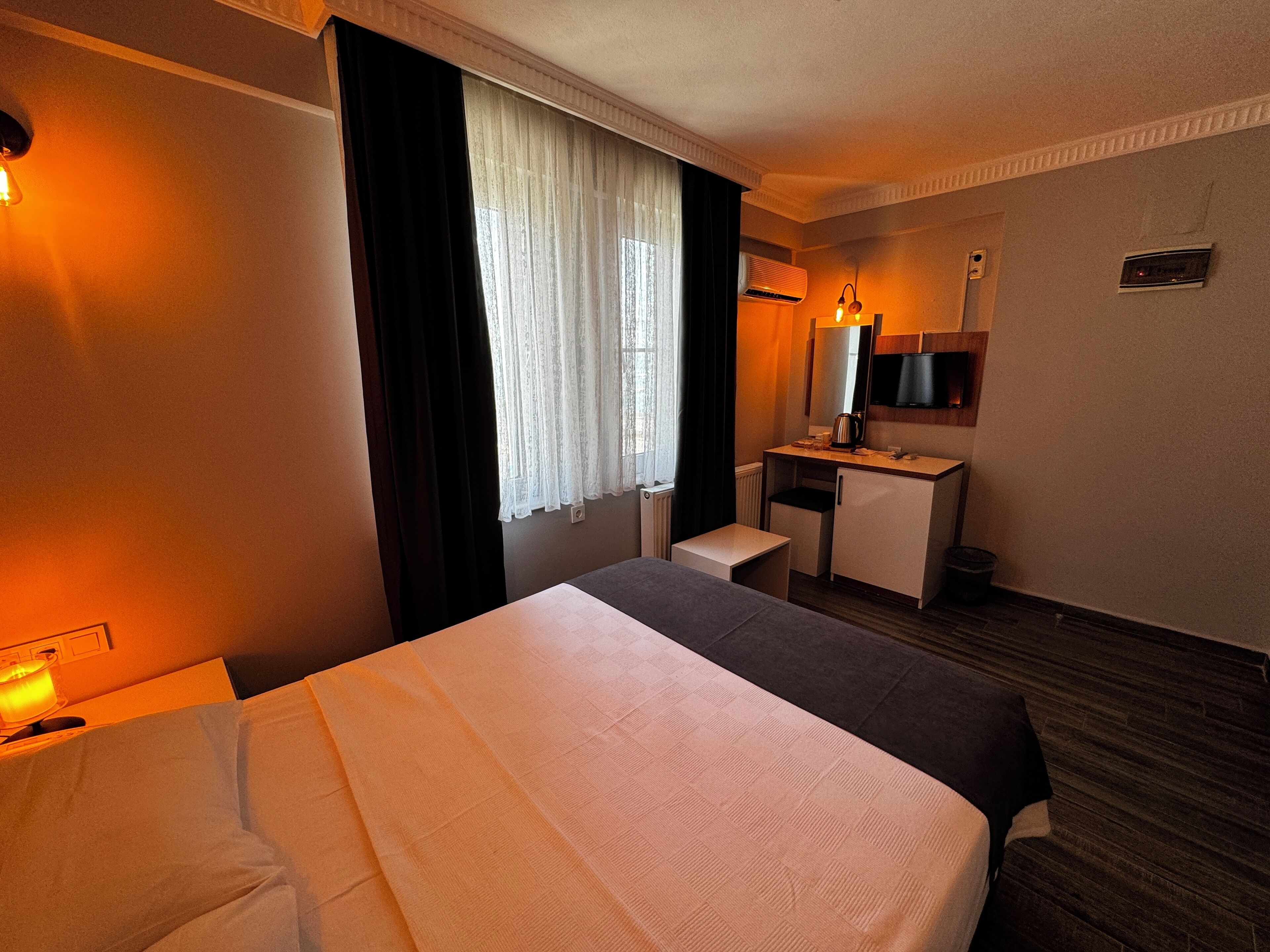 A hotel room with a bed, a desk, a chair, a TV, and a window with curtains.