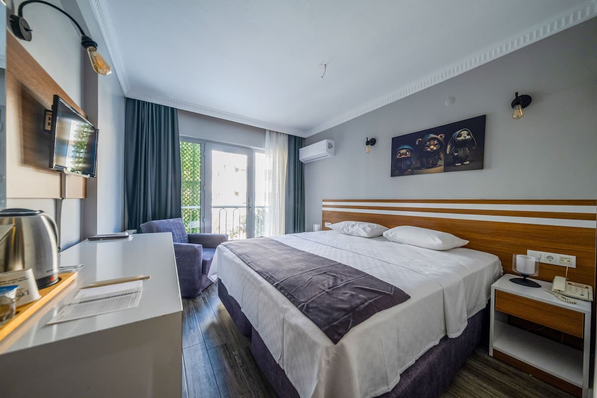 Quarto de hotel com cama, mesa de cabeceira, abajur e vista para o exterior.