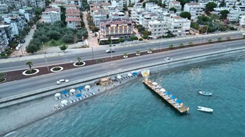 Vista aérea de una ciudad costera con un hotel destacado, un puerto deportivo con barcos y una carretera con vehículos.