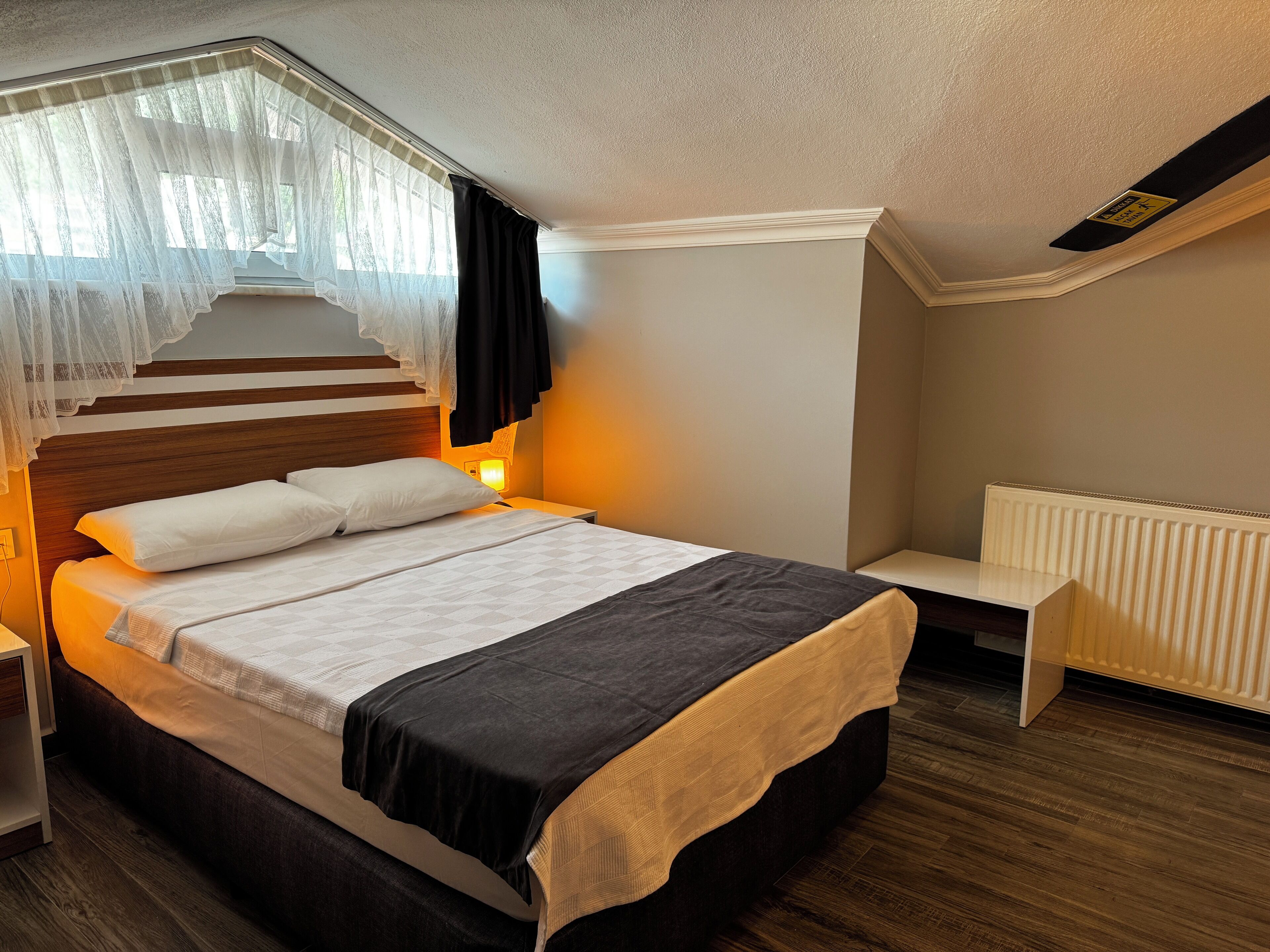 A bedroom with a bed, bedside table, and a window with sheer curtains.