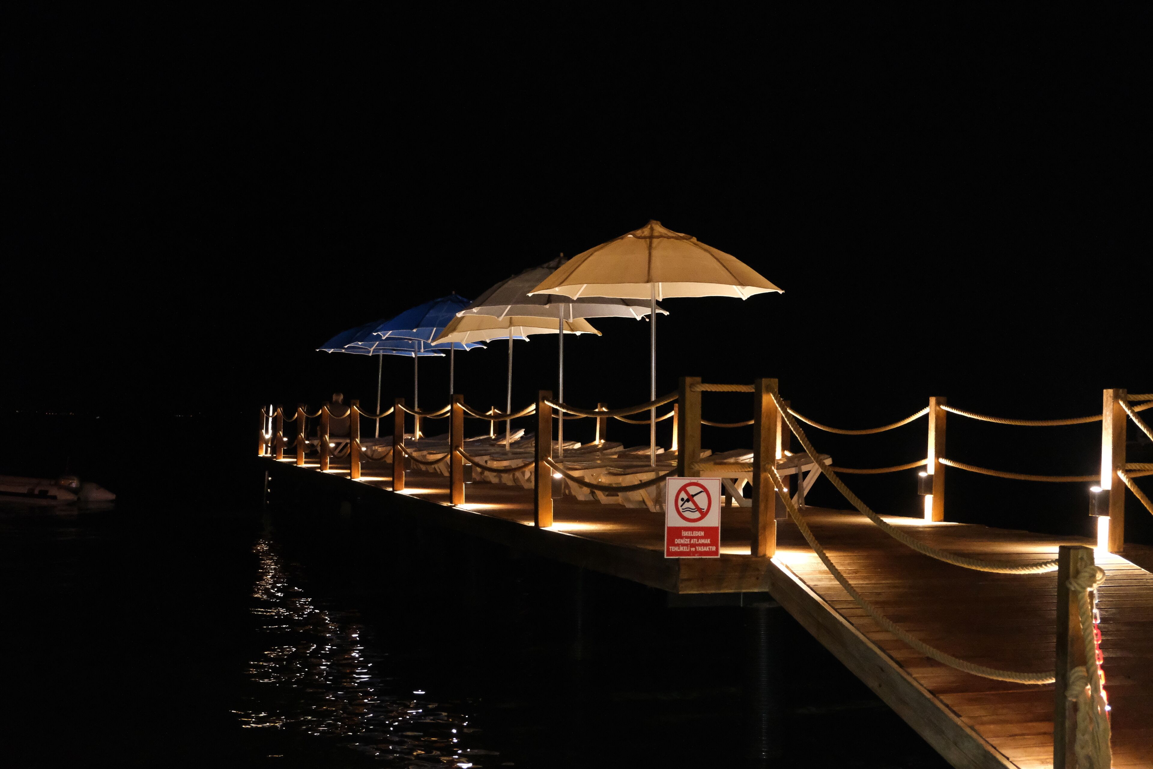 A wooden pier with umbrellas and a no swimming sign.