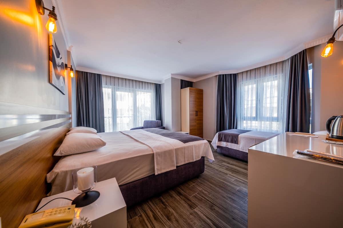 Quarto de hotel com duas camas, uma escrivaninha, uma cadeira, um telefone e um abajur.