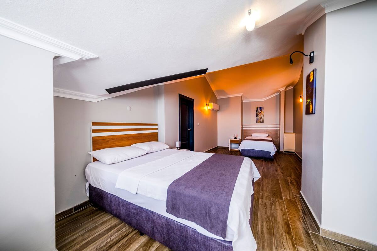Quarto com cama grande, mesa de cabeceira, pia e espelho em banheiro pequeno.