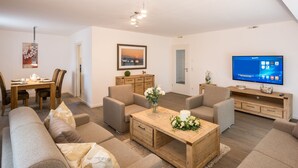 A modern living room with a dining area, a TV, and a wooden coffee table. - Villa Alpenpanorama (Ohlstadt)