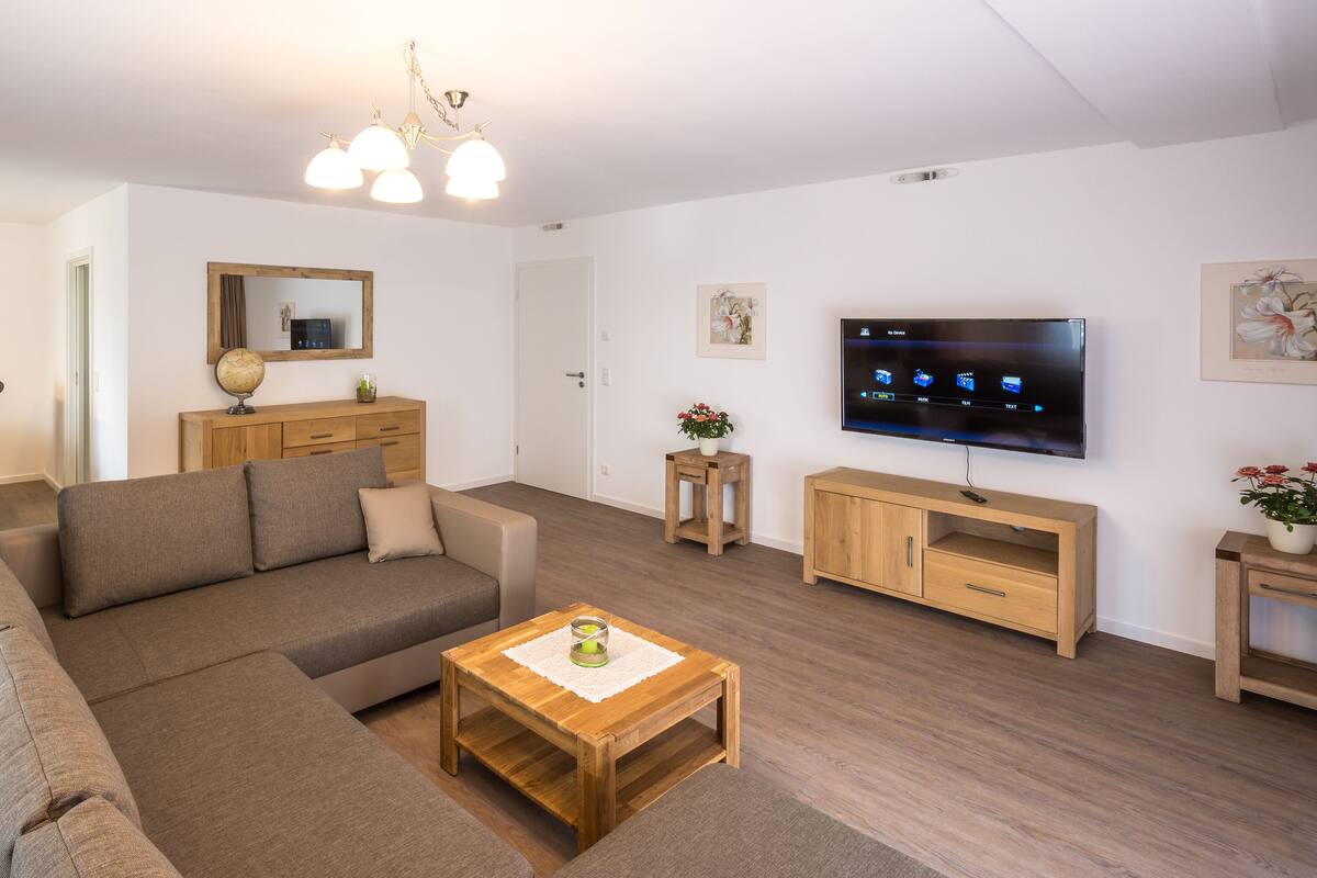 Ein modernes Wohnzimmer mit einer Eckcouch, einem Holztisch, einem Fernseher und einem Essbereich mit Stühlen und Tisch.