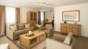 A living room with a sofa, armchairs, a coffee table, a cabinet, and a dining area with chairs and a table. - Villa Alpenpanorama (Ohlstadt)