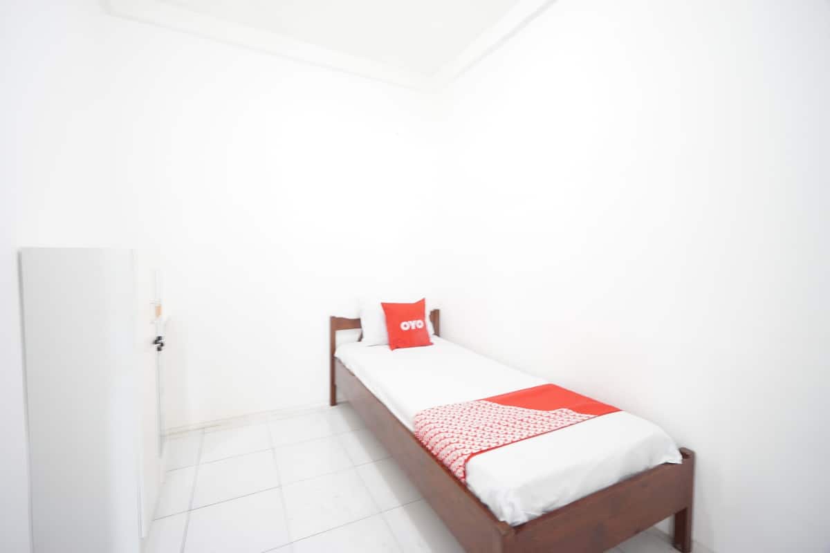Ein kleines Zimmer mit einem Einzelbett, weißen Wänden und einem hölzernen Bettgestell.
