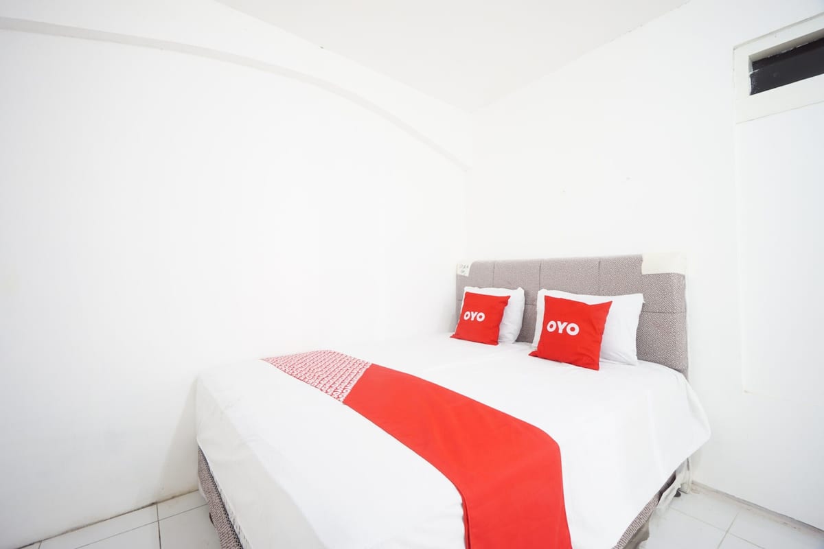 Ein Hotelzimmer mit einem Bett, weißen Wänden und einer roten und weißen Tagesdecke.