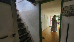 A staircase leading to a room with a green frame door, a person standing in the doorway, and a wall with a number sequence. - SPOT ON 93681 Qodri Homestay Syariah (Surabaya)