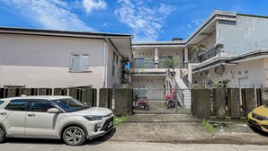 A residential area with a gated entrance, a white car parked in the foreground, and a yellow car in the background. - Hotel O Kost Naura (Somba Opu)