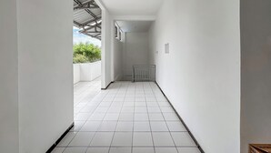 A narrow, tiled corridor with white walls and a metal roof structure. - Hotel O Kost Naura (Somba Opu)