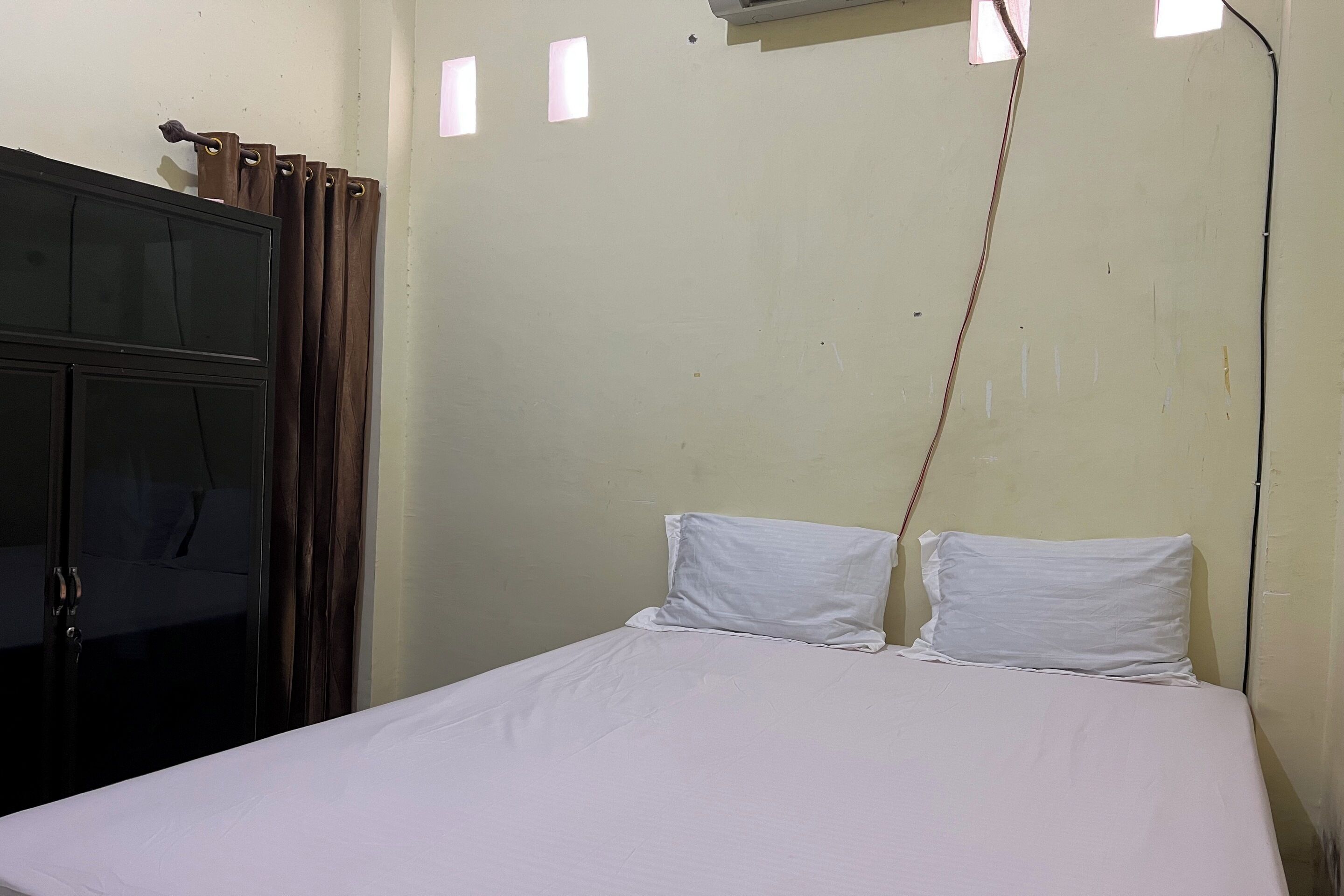 Ein Einzelbett mit weißer Bettwäsche in einem Zimmer mit schlichter Wand und einem Fenster.