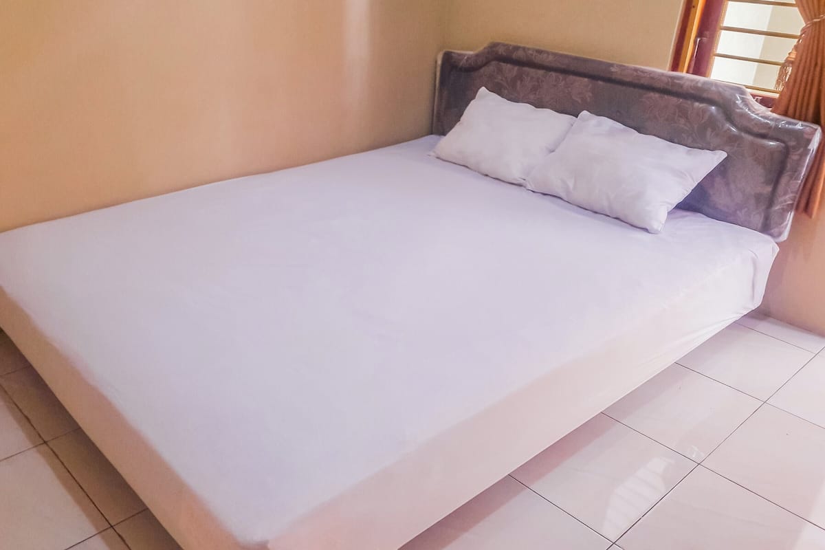 Ein ordentlich bezogenes Bett mit Holz-Kopfschild und weißer Bettwäsche in einem Zimmer mit Fliesenboden.