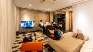 Una sala de estar moderna con un televisor de pantalla plana, un sofá, un comedor y una cocina visible a través de una puerta abierta.