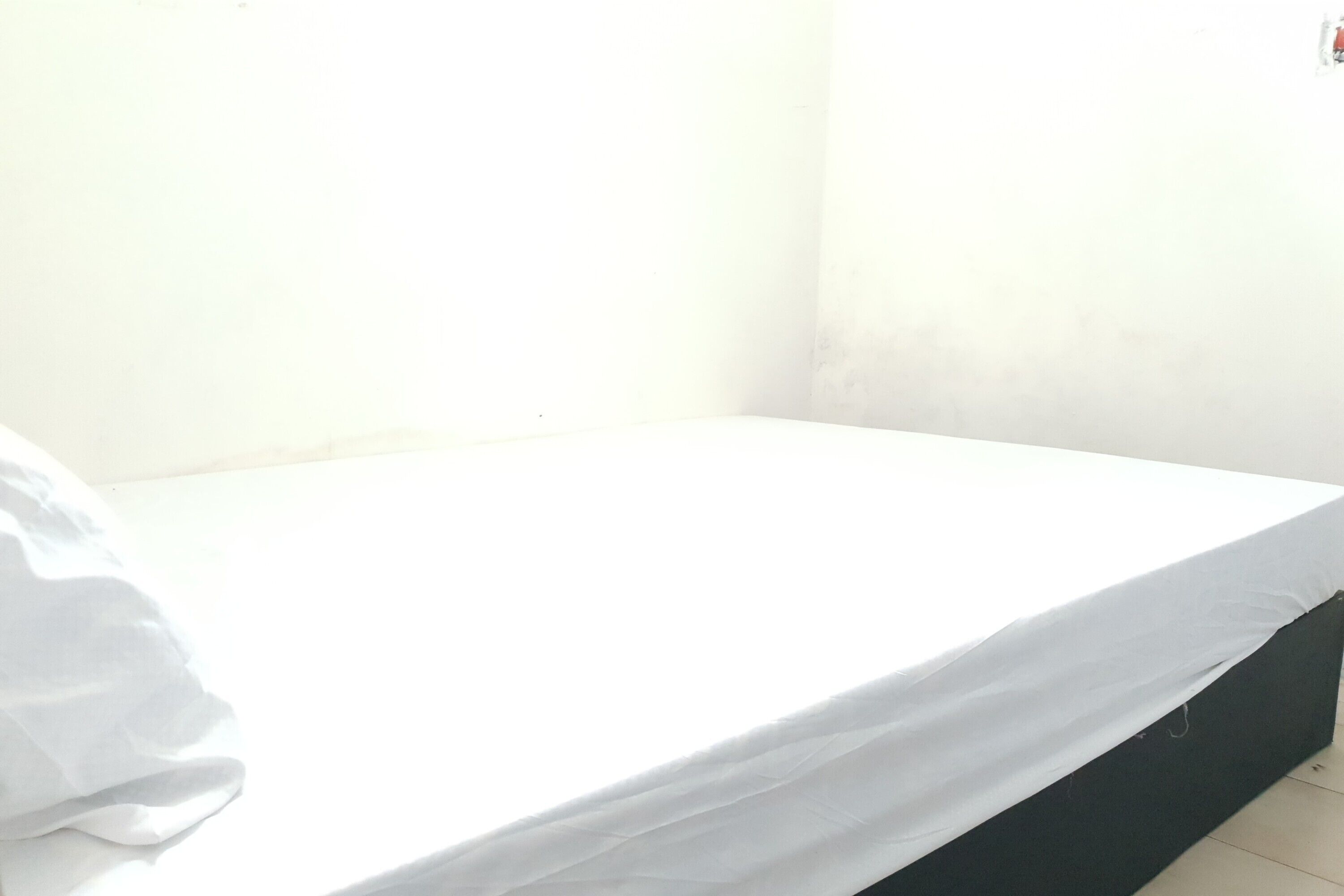 A small, single-bed room with a white mattress and a dark-colored headboard.