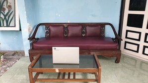 A room with a wooden sofa against a blue wall, a glass coffee table in front, and a door with a geometric design.