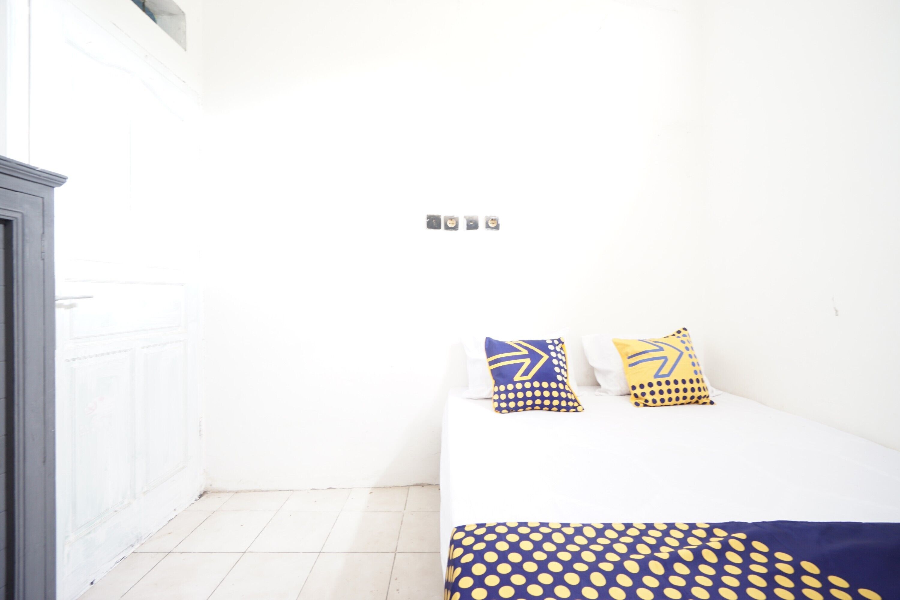 Une petite pièce blanche, avec un lit, deux oreillers et une porte blanche.