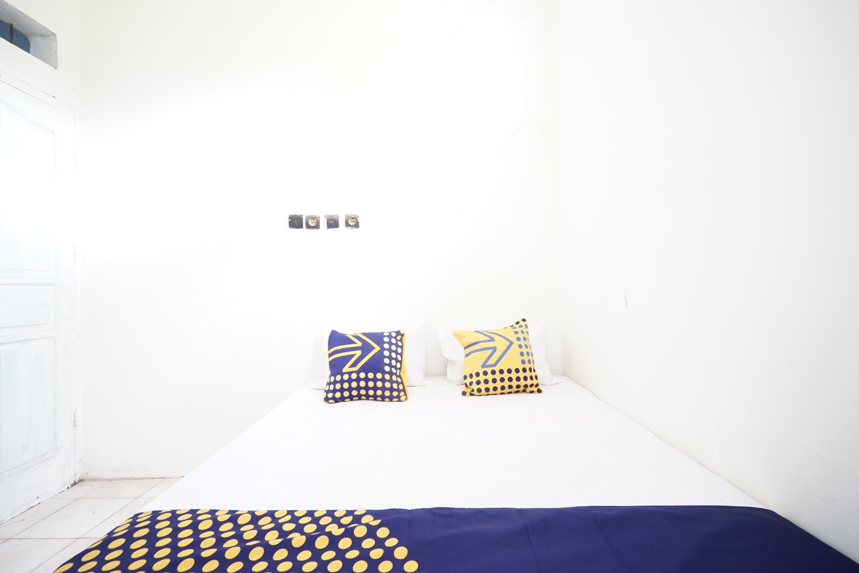 A small, white room with a bed, two pillows, and a patterned blanket.