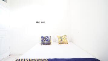 A small, white room with a bed, two pillows, and a patterned blanket.