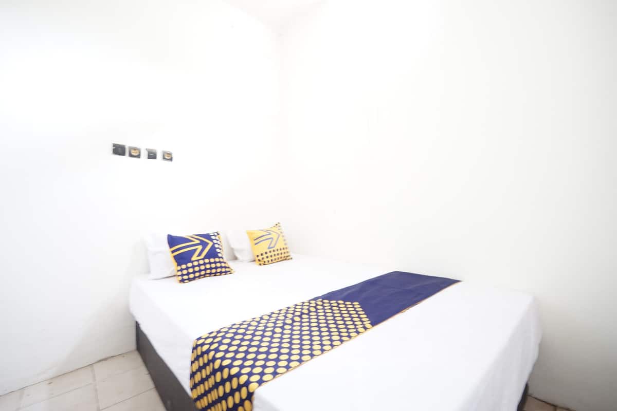 Una cama pequeña y bien hecha con sábana blanca y manta de diseño azul y amarillo.