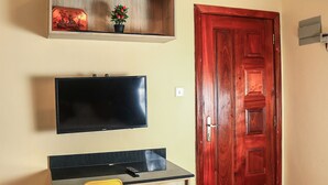 A room with a wooden desk, a mounted TV, a red door, and a shelf with a plant. - South Suites Studios (Nairobi)