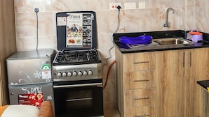A compact kitchen with a stove, oven, microwave, and wooden cabinets. - South Suites Studios (Nairobi)