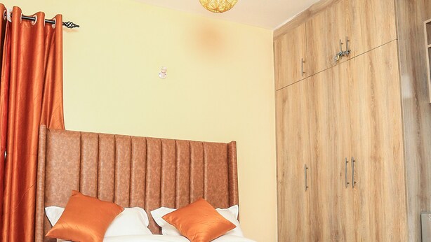 A bedroom with a bed, curtains, a wardrobe, and a hanging light fixture. - South Suites Studios (Nairobi)