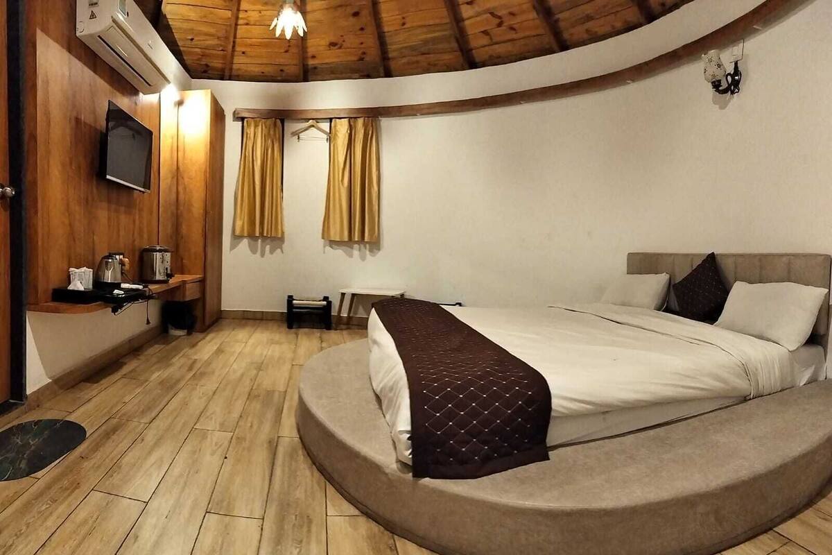 A bedroom with a curved bed, wooden flooring, a small table, a TV, and curtains.