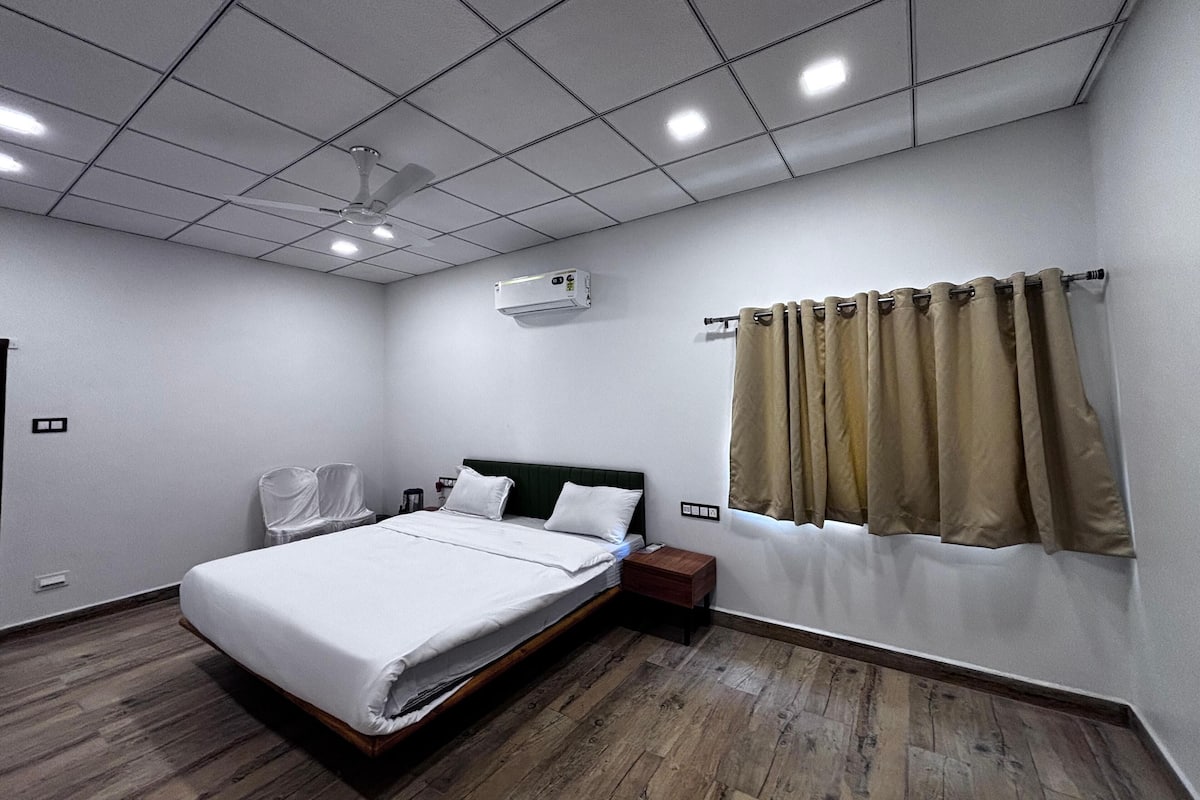 A modern hotel room with a large bed, a ceiling fan, an air conditioning unit, and a window with curtains.