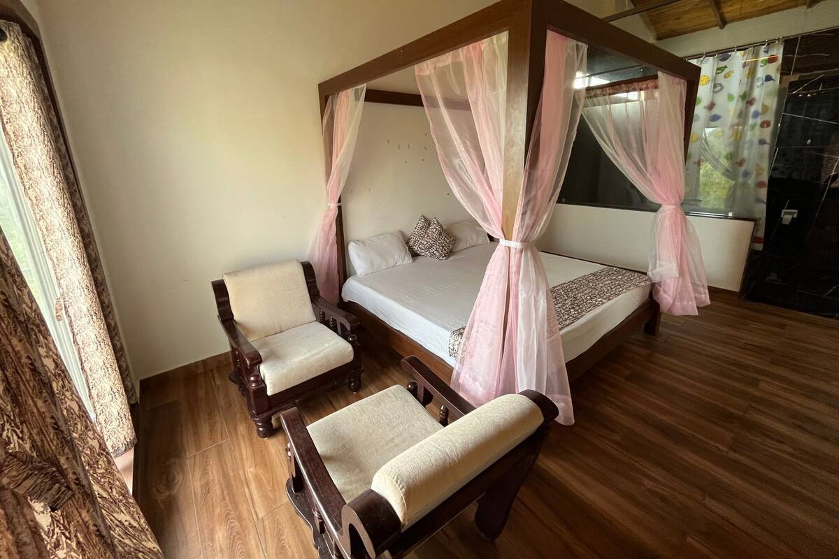 A bedroom with a four-poster bed, two wooden chairs, and a window with curtains.