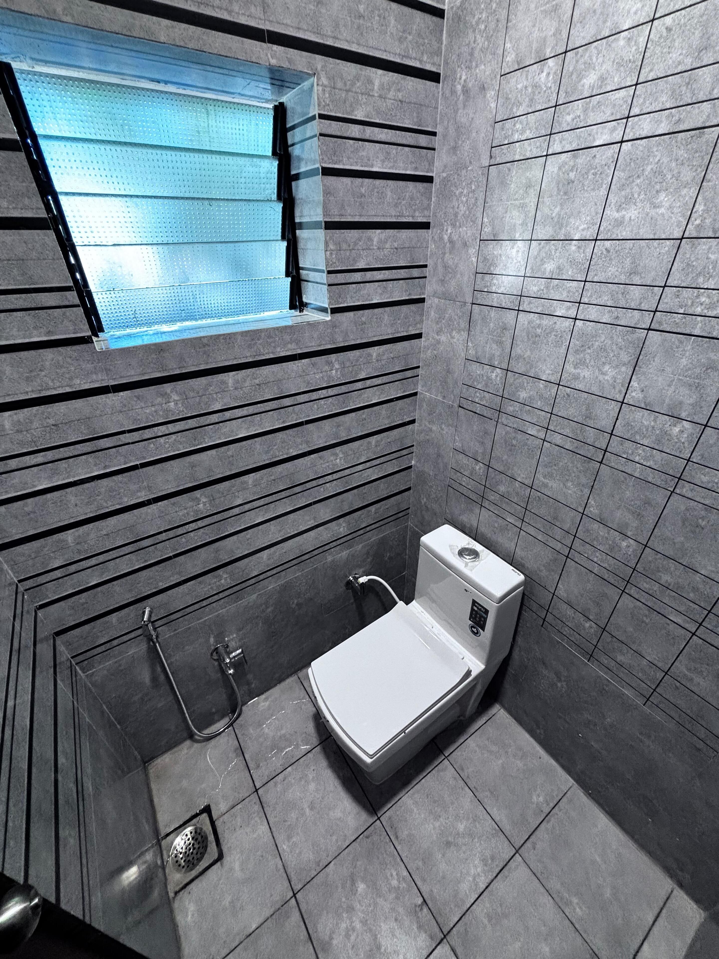 Ein modernes Badezimmer mit Dusche, Toilette und einem Fenster mit Jalousien.