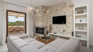 Ein modernes Wohnzimmer mit Steinwand, Kamin, Flachbildfernseher und einer Sitzecke mit Glastisch.