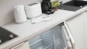 Una cucina con un piano di lavoro bianco, una macchina da caffè, un tostapane e un frigorifero con sportello trasparente.