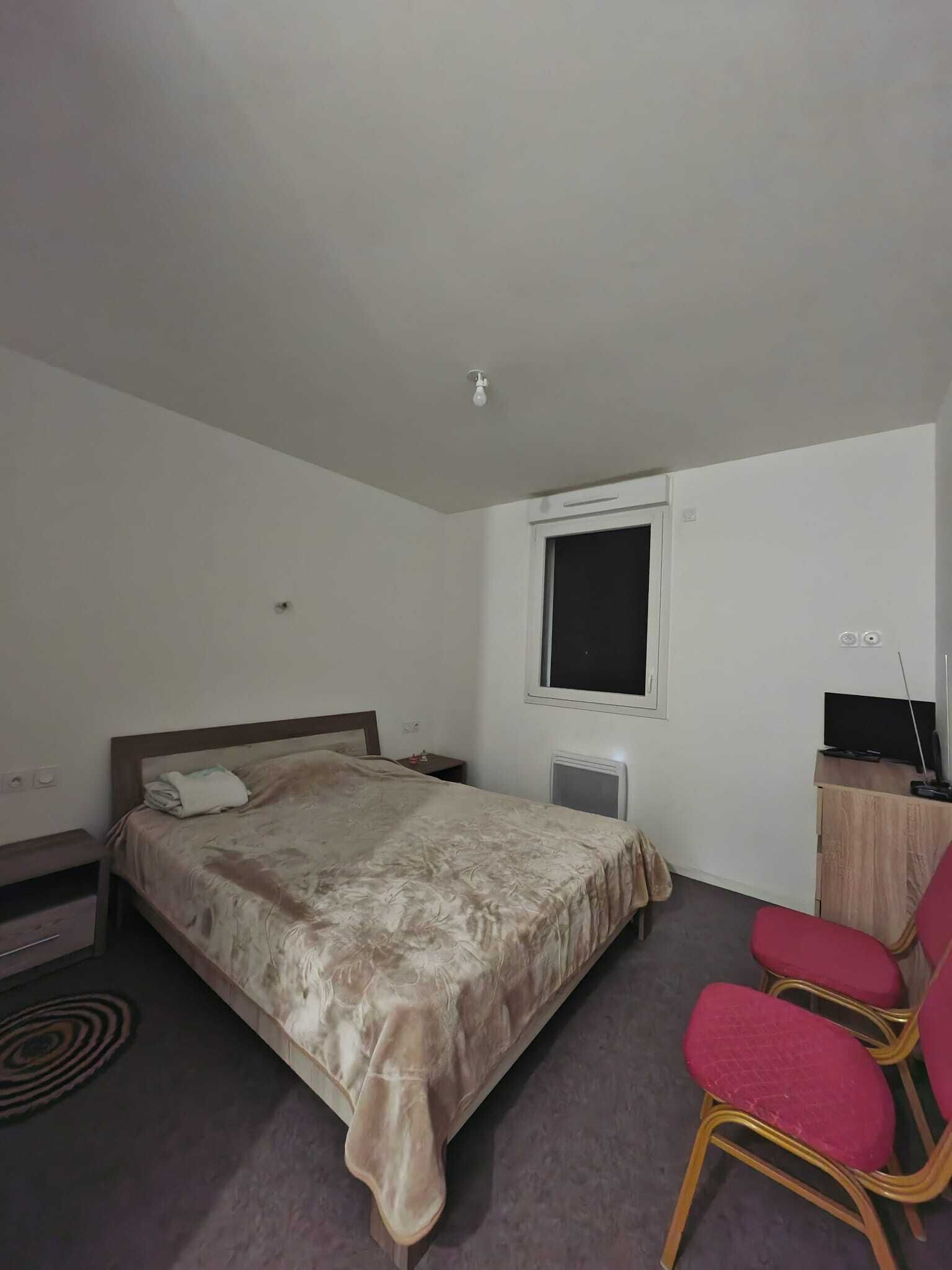 A bedroom with a bed, a desk with a computer, a chair, a window, and a radiator.