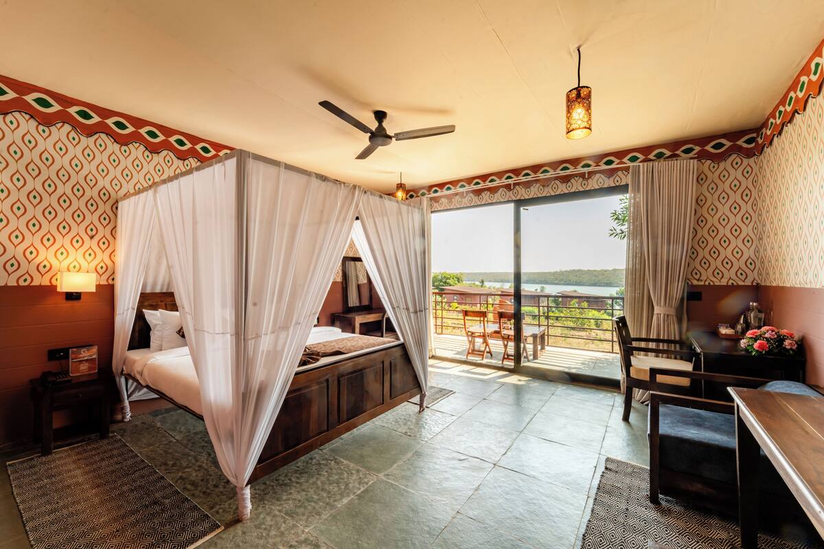 A bedroom with a bed, a ceiling fan, a table, and a view of the outdoors.