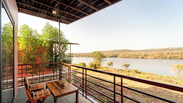 Una mesa y sillas de madera en un balcón con vistas a un lago y árboles.